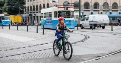 En flicka cyklar &ouml;ver sp&aring;rv&auml;gssp&aring;r. I bakgrunden en sp&aring;rvagn