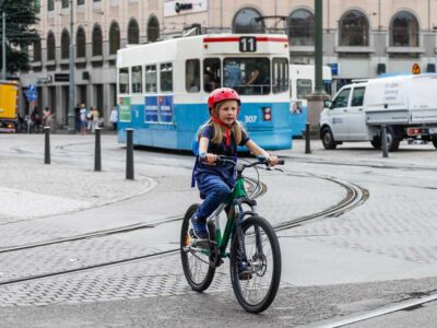 En flicka cyklar &ouml;ver sp&aring;rv&auml;gssp&aring;r. I bakgrunden en sp&aring;rvagn